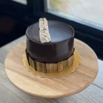 Chocolate glazed cake embellished with gold and icing decoration on wood pedestal