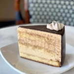 Slice of cake showing layers of white cake and mousse with chocolate glaze