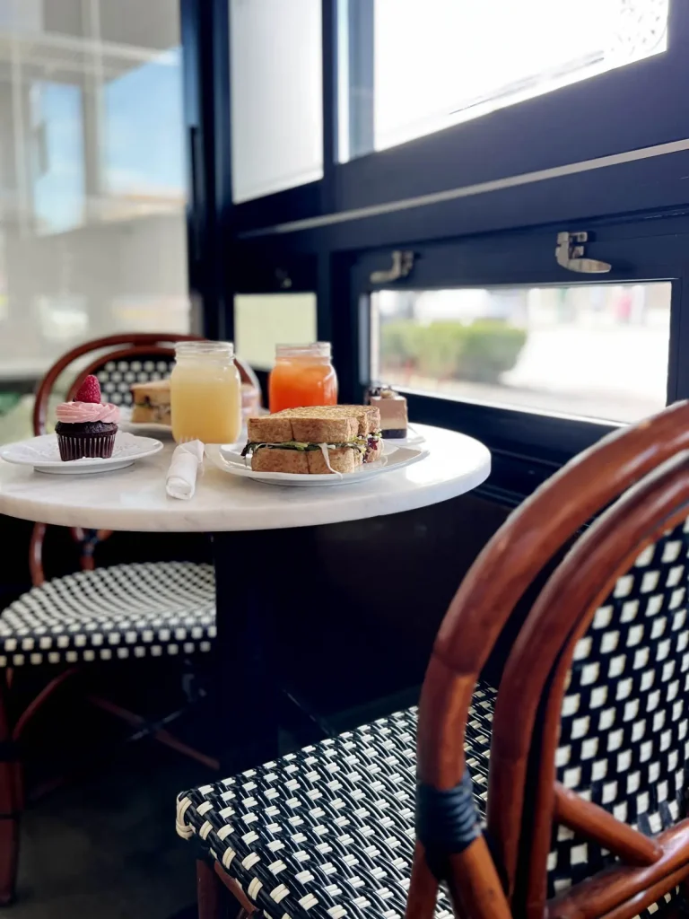 French bistro chairs and marble table with sandwich, cupcake and iced drinks inside Trafiq Cafe & Bakery