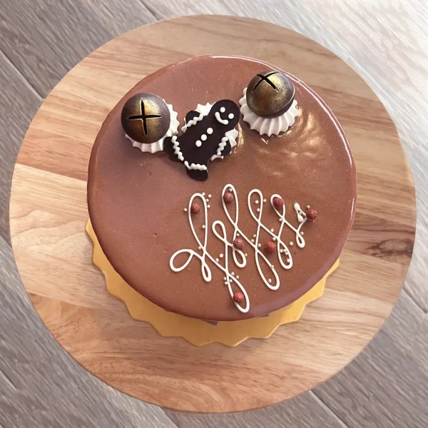 Top of festive Gingerbread cake with fancy white icing, chocolate bells and gingerbread man on chocolate glaze