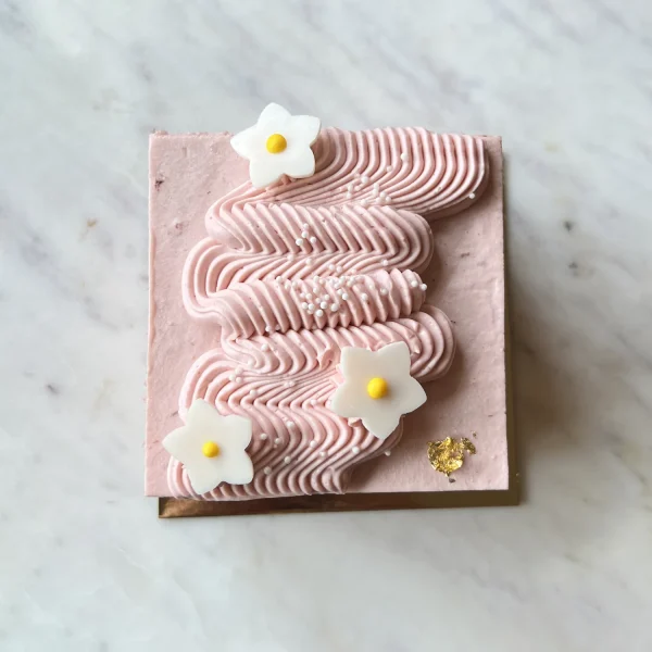 Top-down view of Strawberry Bliss cake — wavy piped strawberry mousse, white fondant flowers with yellow centres, pearl sprinkles and gold leaf.